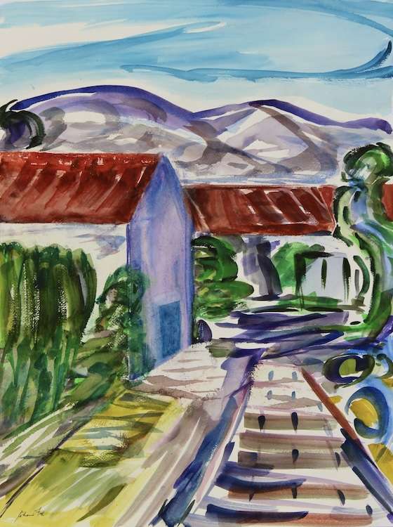 A road through white buildings with red roof, lots of foliage and mountains behind.